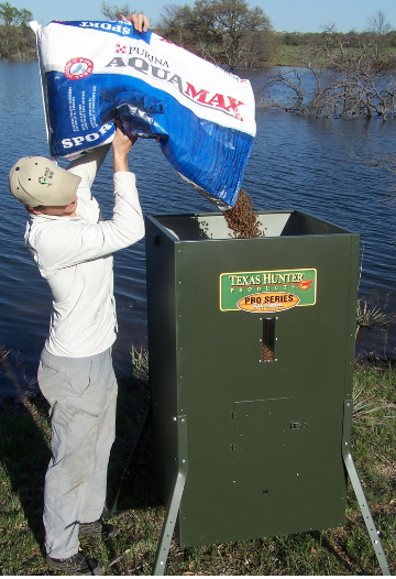 Worker filling fish feeders at pond with AquaMax fish food.